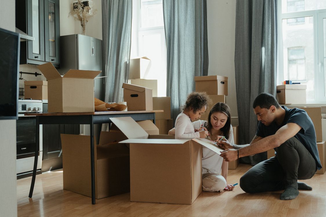 Famille et déménageurs assis par terre dans une cuisine, entourés de cartons et d’objets d’emballage en préparation du déménagement. Famille et déménageurs assis par terre dans une cuisine, entourés de cartons et d’objets d’emballage en préparation du déménagement.