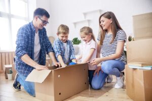 Famille assembleant des cartons de déménagement, enfants et parents heureux, autour d’un grand carton ouvert. Inclut le thème : comment emballer ses affaires pour un déménagement.