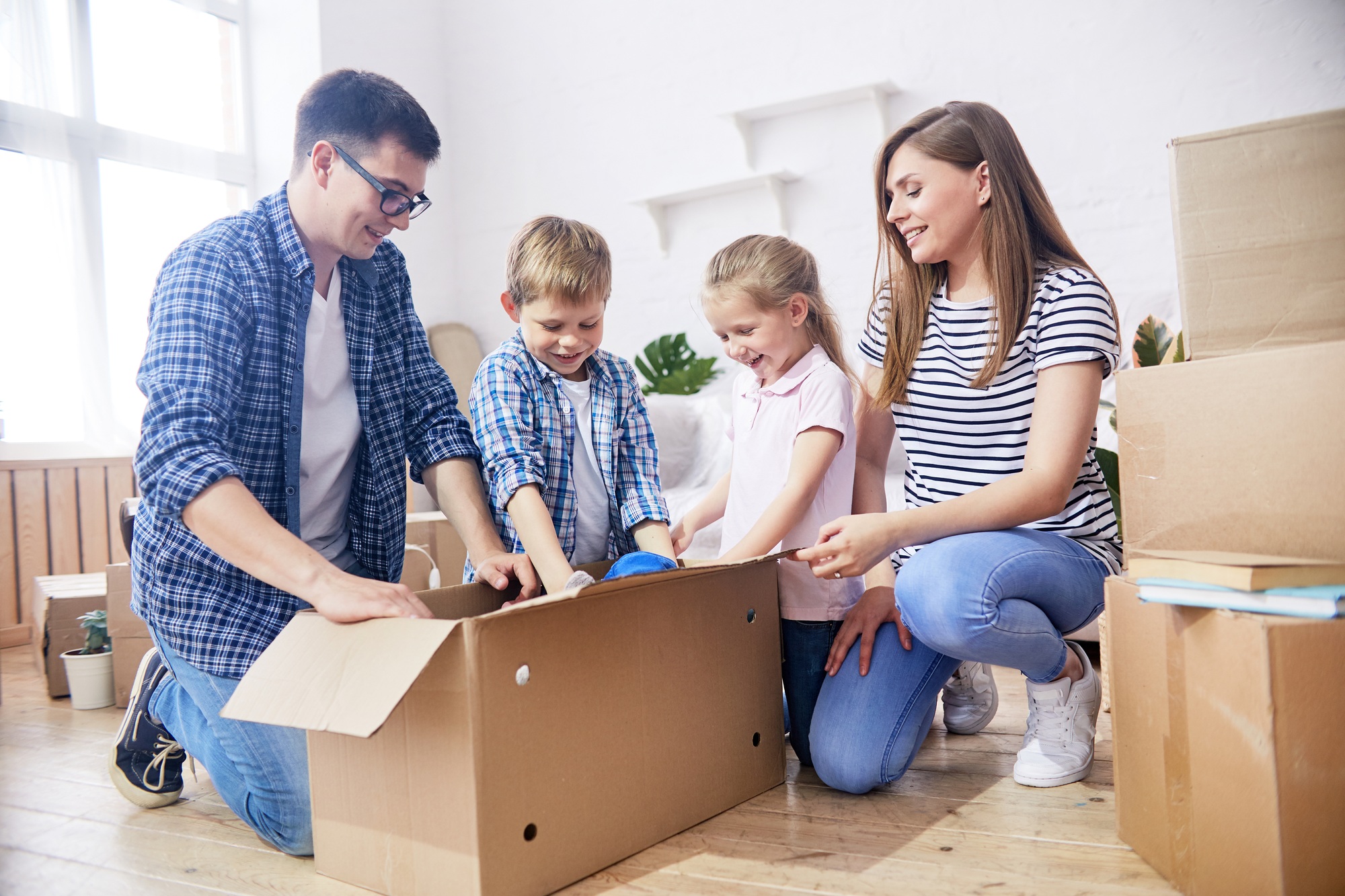 Famille assembleant des cartons de déménagement, enfants et parents heureux, autour d’un grand carton ouvert. Inclut le thème : comment emballer ses affaires pour un déménagement.