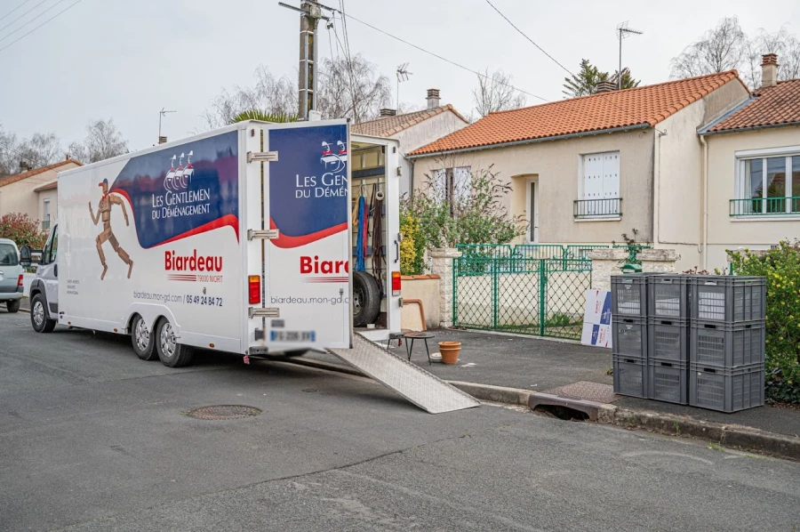 Camion de déménagement avec mechanism de rampe, prêt à charger, dans une rue résidentielle, près de caisses et d’équipements. matériel indispensable pour un déménagement.