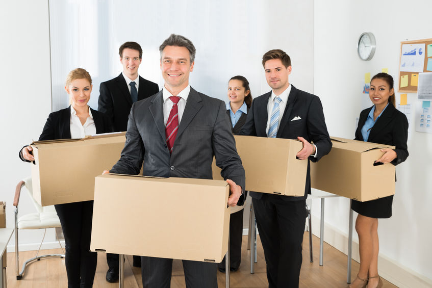 Groupe de six personnes habillées en tenue professionnelle, chacun portant une carton de déménagement dans un bureau.